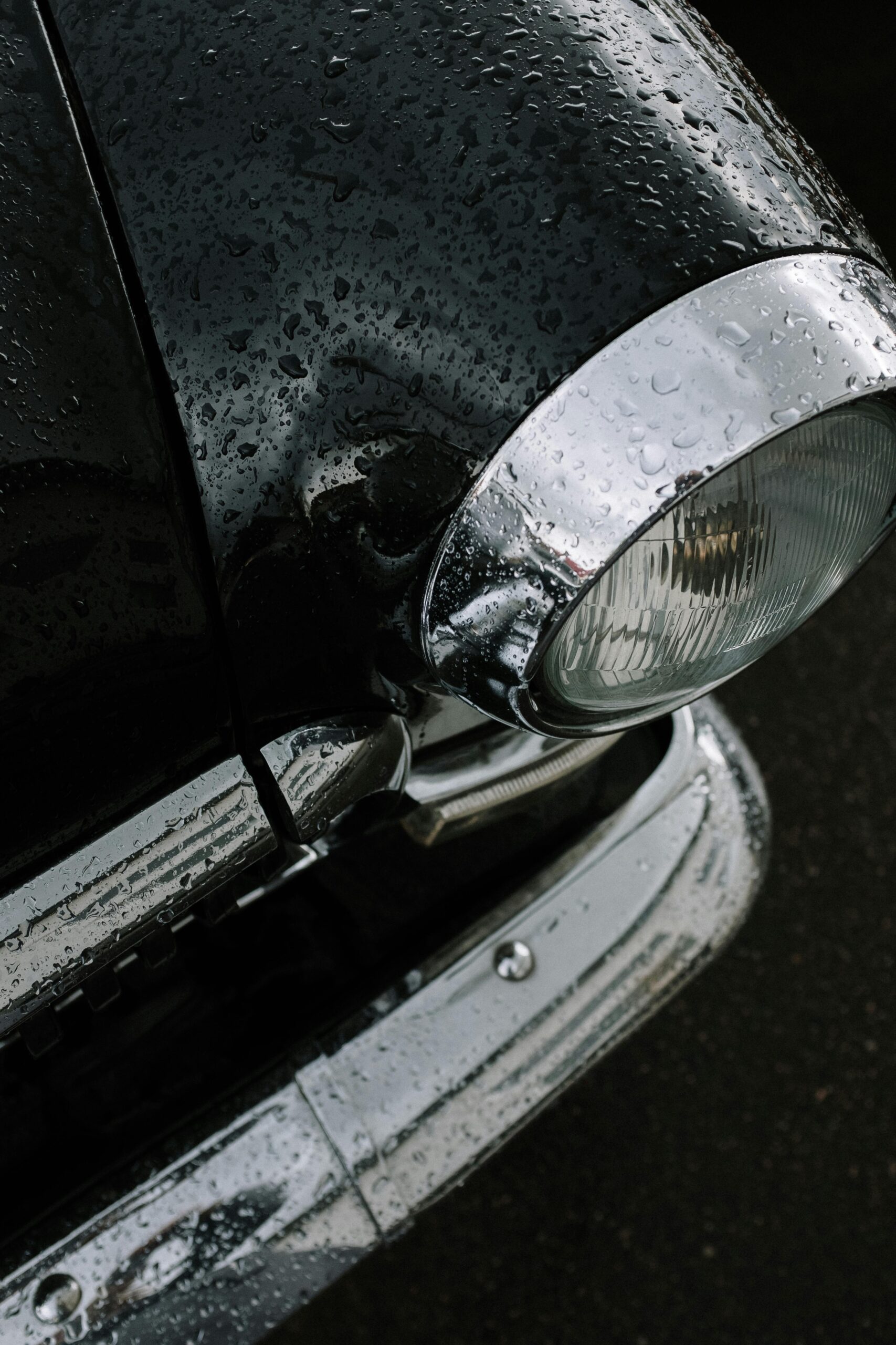 Detailed shot of a vintage car headlight covered in rain droplets, showcasing classic car aesthetics.
